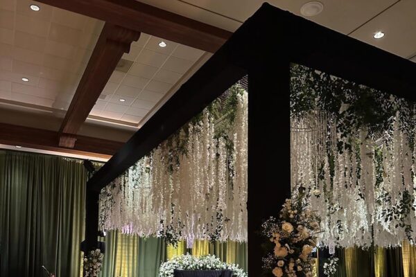Black box truss hung with white wisteria and greenery over a candlelit head table