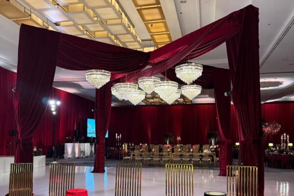 Burgundy velvet draped four-post truss with crystal chandeliers over a white dance floor