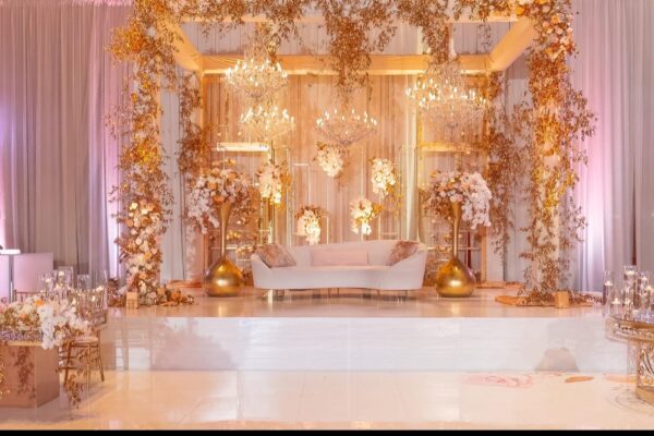 Gold floral-wrapped truss with crystal chandeliers over a white sweetheart sofa on a stage