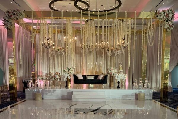 Gold frame truss with hanging white florals and chandeliers over a stage and monogram dance floor