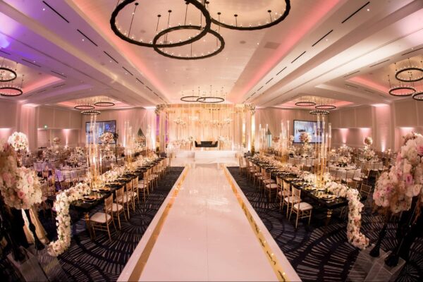 Ballroom with a gold truss stage, white runway dance floor and long floral-lined head tables