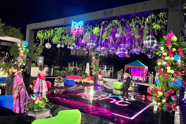 Outdoor black box truss with greenery, disco balls and a neon sign over a printed dance floor